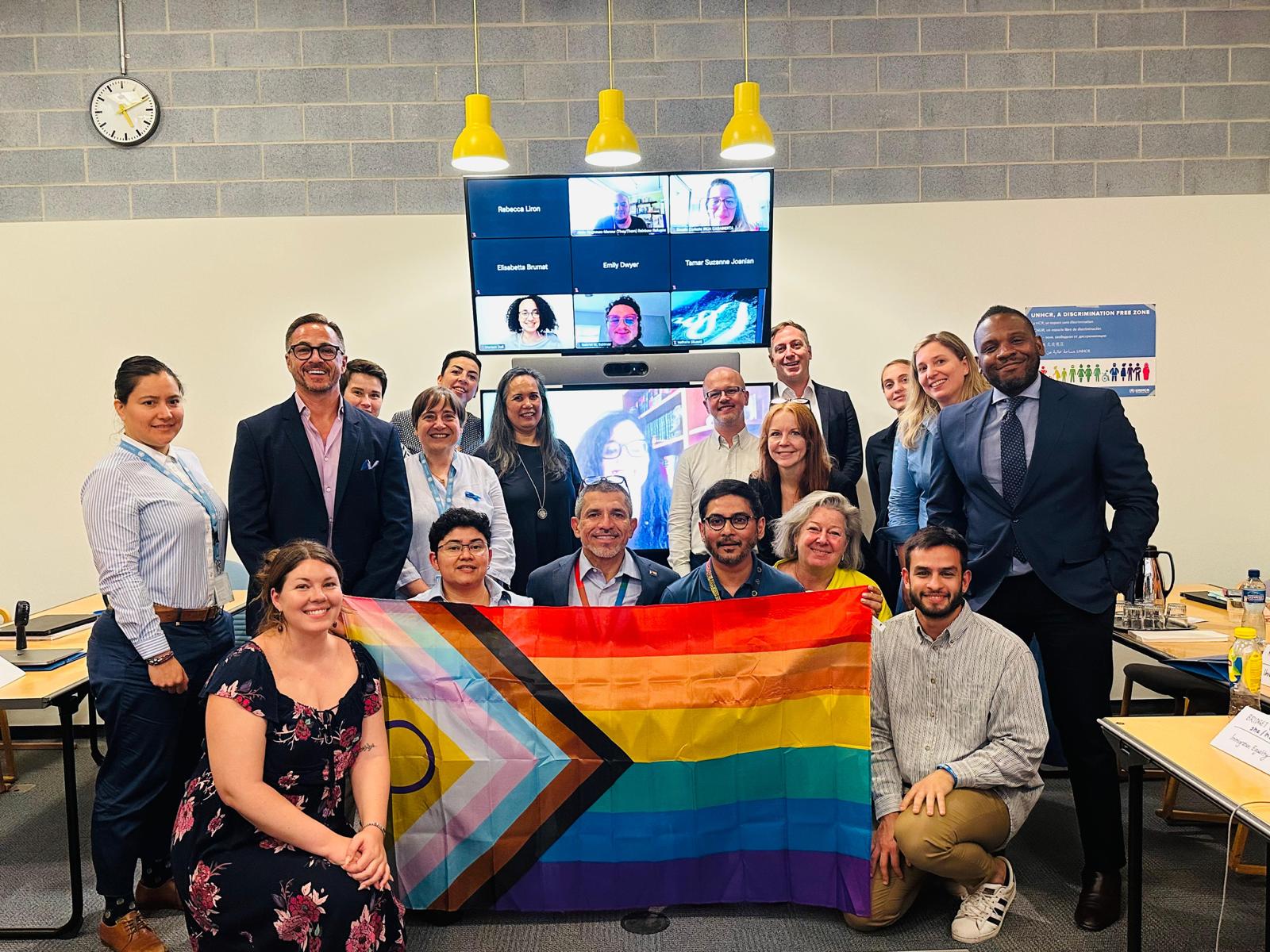 Un grupo de personas en una sala posa para la cámara con una bandera LGBTIQ+
